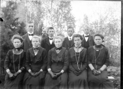 Gruppebilde 1900.  Ytre Enebakk
Konfirmasjonsbilde 5 jenter, 4 gutter. Utendørs, svarte kjoler
Nøkkelord: gruppebilde;konfirmasjon;ytre;gutter;jenter;kjoler;dress;pyntet;utendørs;tre;smykker