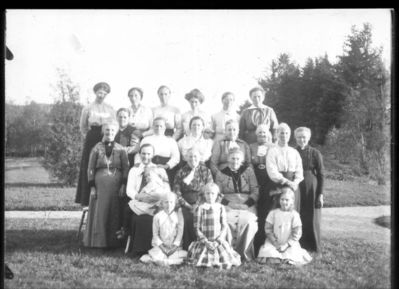 Gruppebilde  1900 - 10
Søtten eldre kvinner, fire barn, oppstilt utendørs. Sommer
Nøkkelord: gruppe;barn;kvinner