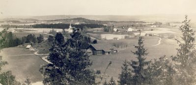 Enebakk kirke midt i bilde;
Nøkkelord: landsakp;enebakk;enebakkkirke;kirke;kirkebygda;tre;trær;jorde;gård;gårdsbruk;skole;hus;bygninger